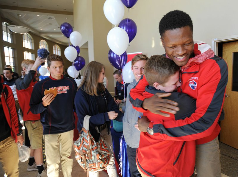 SK Shittu (right) of Providence Academy in Rogers gets a hug from Stewart Bivens, 14, on Thursday after signing to play basketball for the University of Central Arkansas during a signing ceremony at Rogers First Church of the
Nazarene.