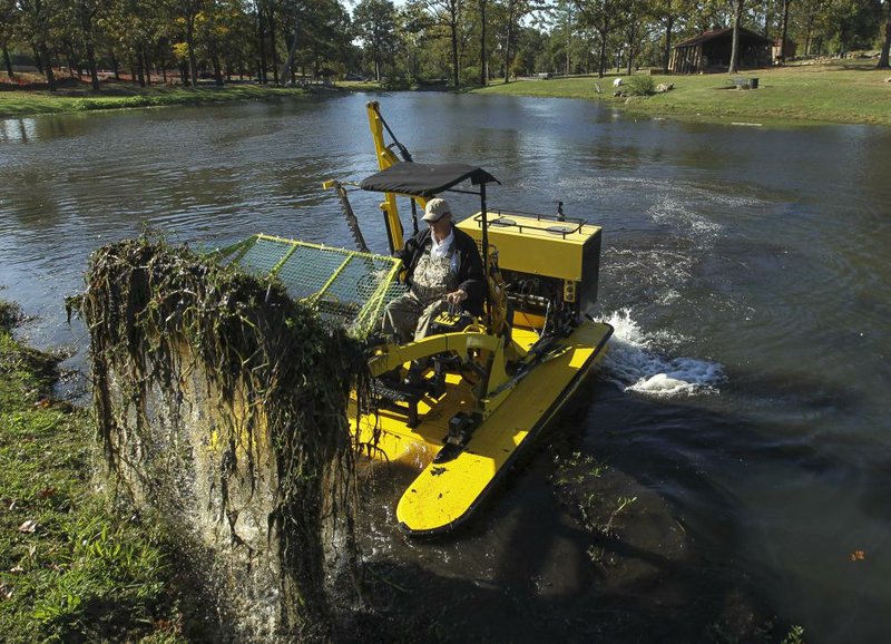 Roddy McCaskill scoops weeds Wednesday from the fishing pond at War Memorial Park with his Weedoo TigerCat boat. 