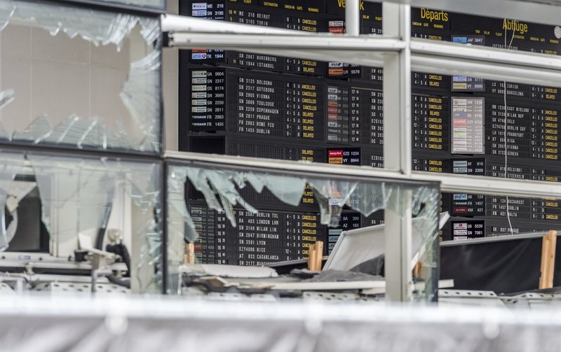 In this March 23, 2016 file photo, an arrivals and departure board is seen behind blown out windows at Zaventem Airport in Brussels.