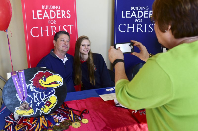 Providence Academy senior Anna Siemens (center) takes a photo with her father David Siemens on Tuesday after signing a track scholarship with Kansas University at First Nazarene Church in Rogers.