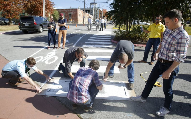 Mike Lydon (right), with Street Plans Collaborative of Miami, Fla., holds a stencil in place Thursday as the last part of a crosswalk is painted on Spring Street in Fayetteville.