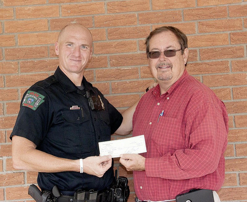 LYNN KUTTER ENTERPRISE-LEADER David Faught, school resource officer with Prairie Grove Police Department, accepts a donation from Mayor Sonny Hudson on behalf of the Prairie Grove Lions Club. The money will go to the 2016 Shop with a Cop.