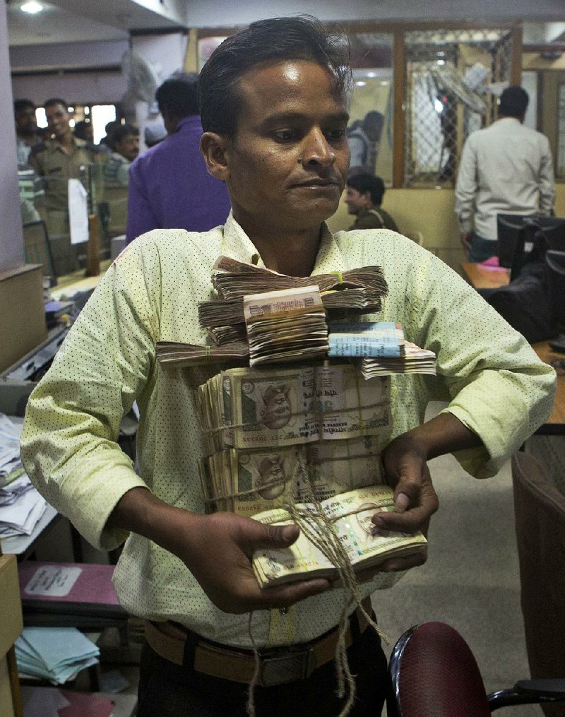 A bank worker in Allahabad, India, carries bundles of discontinued rupee bills that were deposited by customers in this Nov. 13 photo. Visa Inc. and Mastercard Inc. stand to benefit from the Indian government’s decision to remove high-denomination bills from circulation.