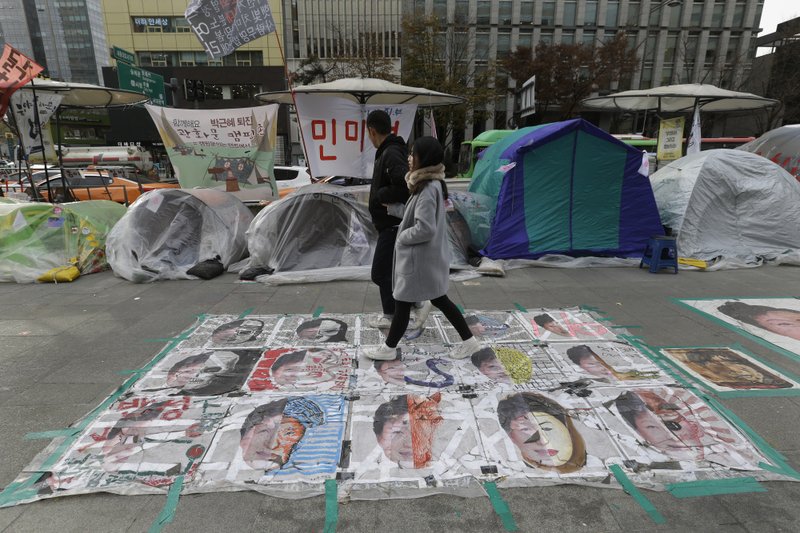 A couple walks over paintings critical of embattled South Korean President Park Geun-hye on a street in Seoul on Wednesday.