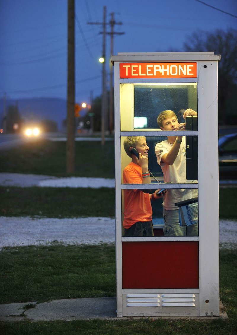 Mason McCourt, 13, (left) and Blake Williams, 14, both of Prairie Grove, use a telephone booth in the city in this 2015 photo. The phone booth, which is on the National Register of Historic Places, now offers free local calls.