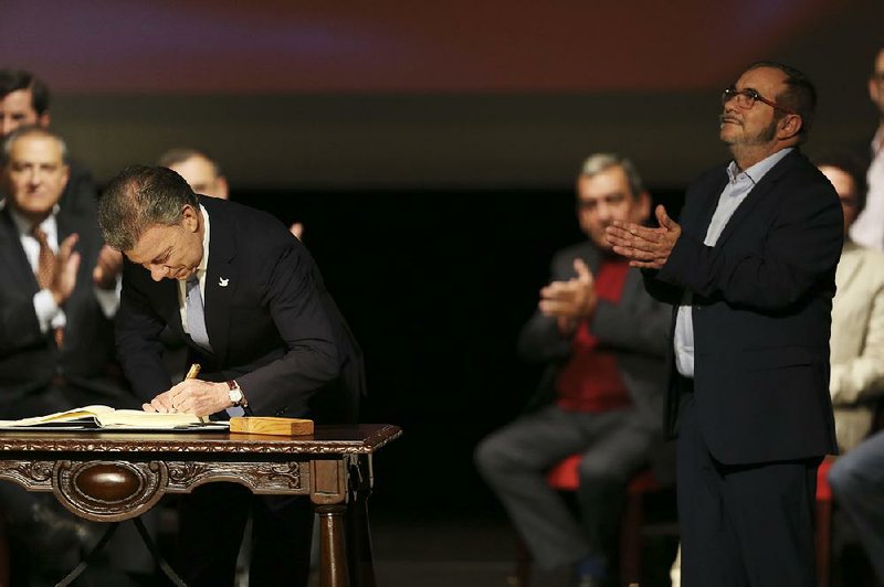 Rebel leader Rodrigo Londono (right) applauds Thursday as Colombian President Juan Manuel Santos signs a modifi ed peace accord with rebels of the Revolutionary Armed Forces of Colombia during a ceremony in Bogota.