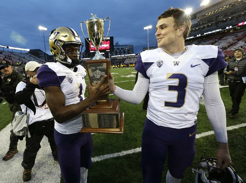 Washington quarterback Jake Browning (right) hands the Apple Cup Trophy to wide receiver John Ross as they walk off the fi eld Friday after the No. 5 Huskies defeated No. 23 Washington State 45-17 in Pullman, Wash. Browning passed for 292 yards and 3 touchdowns in the victory, while Ross had 8 catches for 80 yards and 1 touchdown.