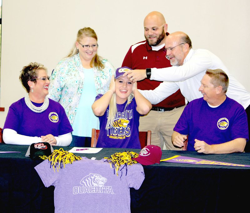 MARK HUMPHREY ENTERPRISE-LEADER Lincoln senior Lexington Dobbs laughs as athletic director Deon Birkes adjusts an Ouachita Baptist University softball cap for her. Dobbs accompanied by her parents, Dwayne and LaDonna Dobbs, of Lincoln, signed a national letter of intent to play women&#8217;s college softball at OBU Nov. 14. Looking on are Lincoln softball coaches, Megan Jobe (left) and Beau Collins.