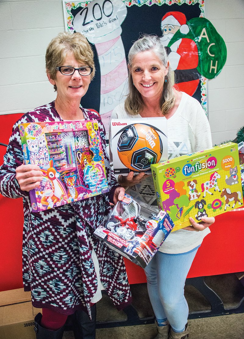 Donna Moorehead, left, and Karen Wynne hold donated toys near the sleigh in the main entrance of Pangburn Middle School, where toys have been collected for Festival of Stars, a toy drive for Arkansas Children’s Hospital.