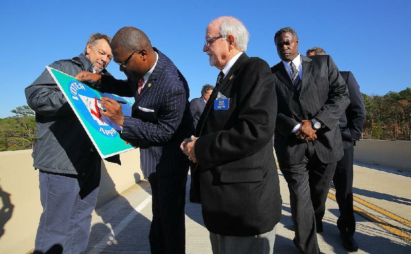 Glenn Bolick (left) of the Arkansas Highway and Transportation Department holds a placard Wednesday as state Highway Commissioner Frank D. Scott Jr. signs it at an event on the Norman Road Interstate 40 overpass in North Little Rock celebrating completion of the $38.4 million I-40 widening project. Waiting to sign are commission Chairman Dick Trammel (center) and Emanuel Banks, the Highway Department’s deputy director and chief engineer.