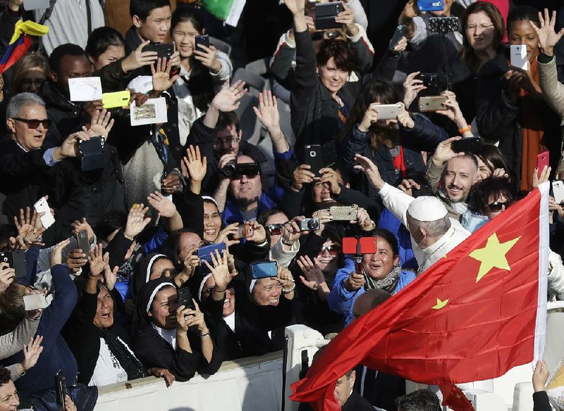 Pope Francis is framed by a Chinese •ag as he greets the crowd after Mass at the Vatican. Francis is continuing talks with China in an effort to improve relations between the Holy See and the Communist country.