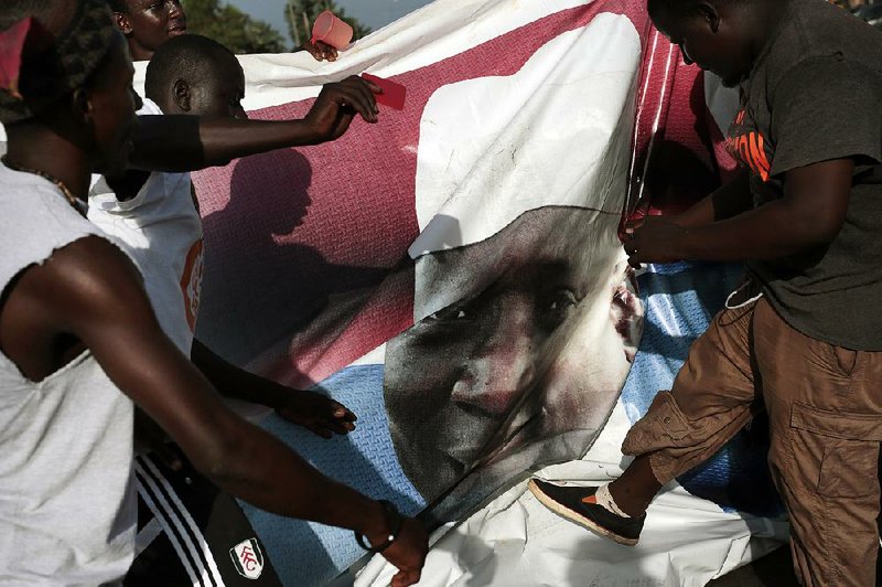 Gambians celebrating the victory Friday of opposition candidate Adama Barrow tear down a poster of longtime President Yahya Jammeh in the city of Serrekunda.