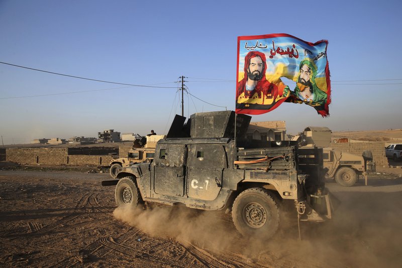In this Sunday, Nov. 27, 2016 photo, an Iraqi special forces humvee passes with a Shiite flag bearing the likeness of Imam Hussein and Imam Ali with Arabic words reading "At your service Hussein" in the front line neighborhood of Bakr, in Mosul, Iraq. 