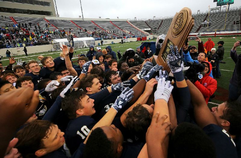 Pulaski Academy players hold up the championship trophy after the Bruins won their third consecutive state title by knocking off Wynne 55-16 in the Class 5A fi nal on a cold, rainy Saturday afternoon at War Memorial Stadium in Little Rock.