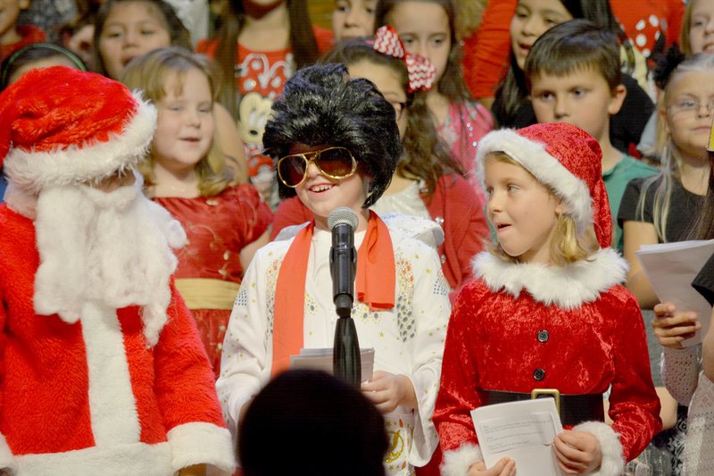 Amy Thomas/Special to Siloam Sunday Allen Elementary students, from left, Caleb Marksberry (Santa Claus), Tolley Blanchard (Elvis) and Jane Anglin (Mrs. Claus) led all second-grade students in a song Tuesday in the school&#8217;s annual Christmas program held at the Cathedral of the Ozarks at John Brown University.