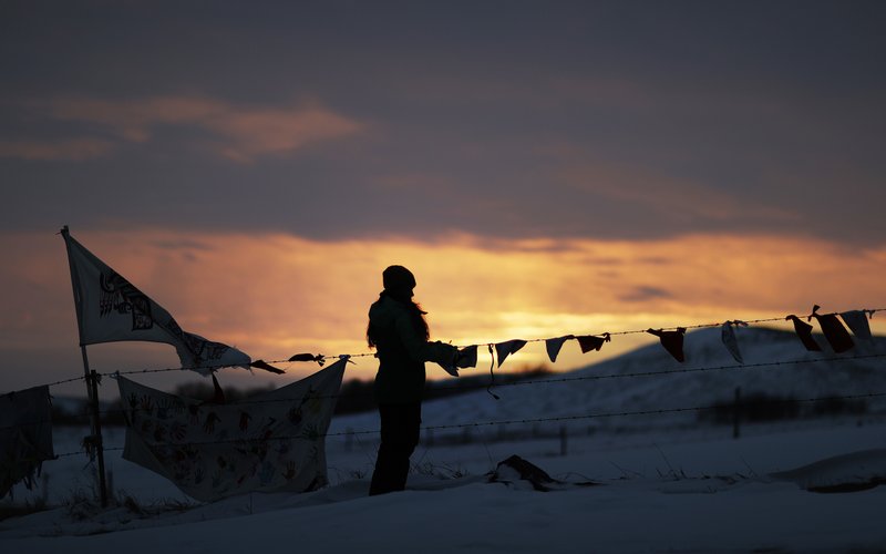 A woman watches the sunset at the Oceti Sakowin camp where people have gathered to protest the Dakota Access oil pipeline in Cannon Ball, N.D., Friday, Dec. 2, 2016. Hundreds of protesters fighting the Dakota Access pipeline have shrugged off the heavy snow, icy winds and frigid temperatures that have swirled around their large encampment. (AP Photo/David Goldman)