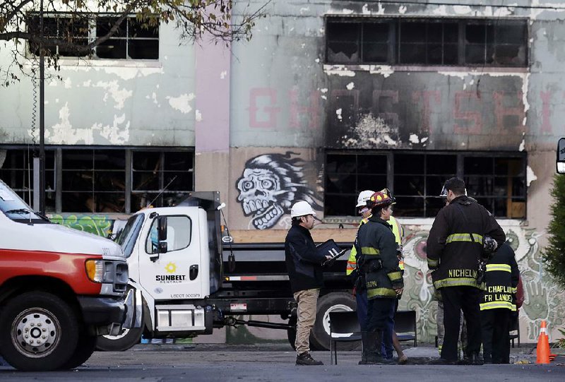 Emergency crews work in front of the site of a warehouse fire, Monday, Dec. 5, 2016, in Oakland, Calif. The death toll in the Oakland warehouse fire climbed Monday with more bodies still feared buried in the blackened ruins, and families anxiously awaited word of their missing loved ones. (AP Photo/Marcio Jose Sanchez)