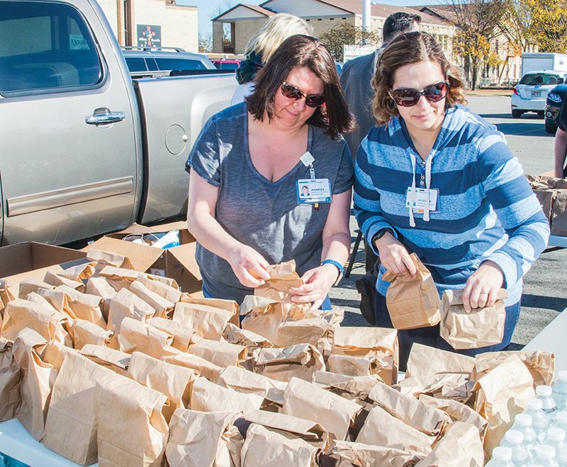 Jennifer Ward, left, and Jacquelyn Hoyle, senior laboratory technologists with Baptist Health Medical Center-Conway, sort sack lunches prepared by hospital employees for the community outreach event held Friday in Conway. Lunches, bottled water, cold-weather clothing items and tarps were distributed to those in need.