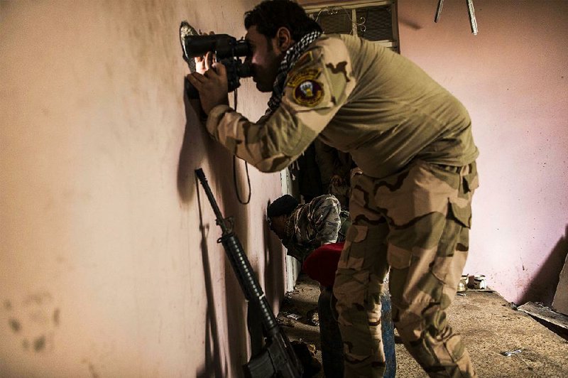 An Iraqi soldier from the 9th Division looks through a sniper hole Monday in the al-Intisar district in Mosul, Iraq.