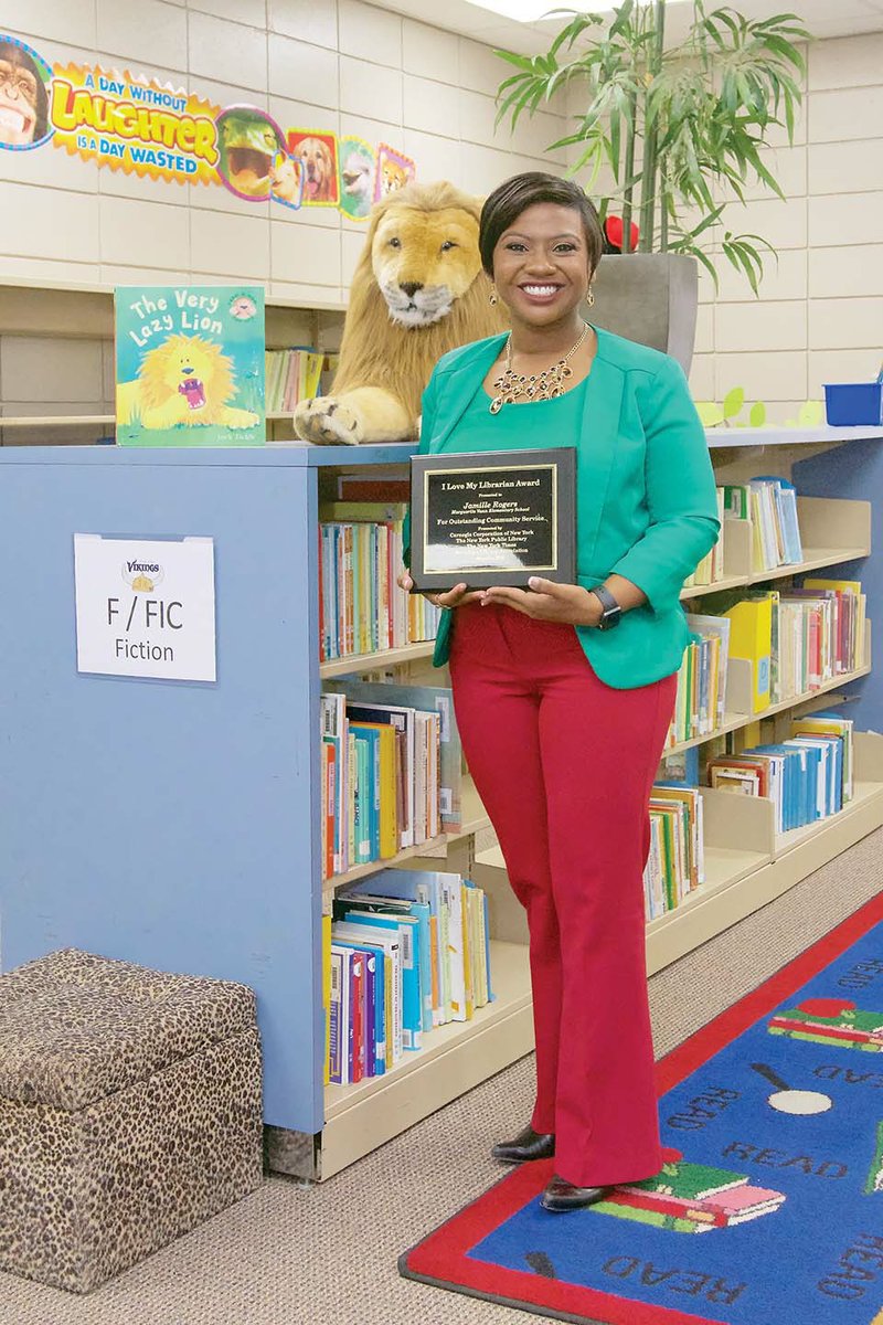 Jamille Rogers, library media specialist for Marguerite Vann Elementary School in Conway, stands in the media center. She said the room was boring when she took the position, but she enlivened it with a safari theme. Rogers, 34, was one of 10 national winners of the I Love My Librarian Award, which came with a plaque, which she is holding, and a $5,000 prize. Rogers said she plans to use the money to raise $25,000 to take the library “to the next level.”