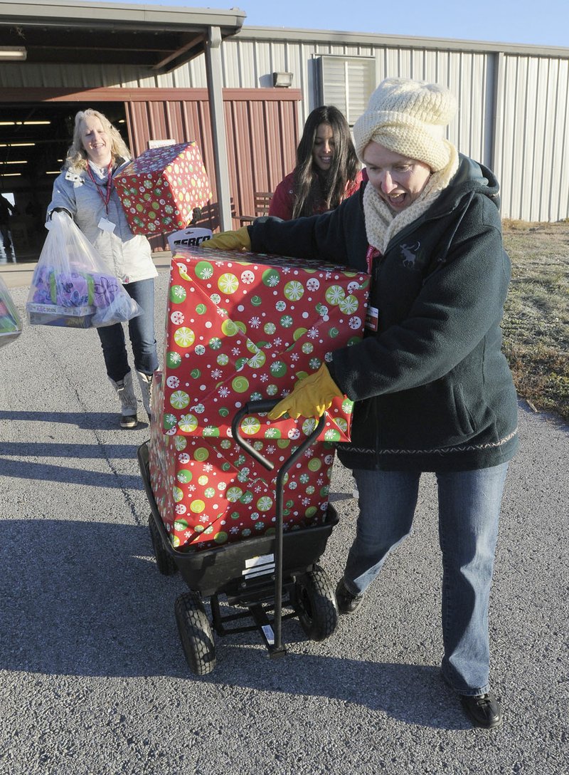 Volunteers Virginia Higginbotham (left) and Nancy Albin (right) deliver gifts Friday during Sharing & Caring at the Benton County Fairgrounds near Bentonville.