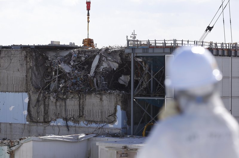 In this Feb. 10, 2016 file photo, a member of the media tour group wearing a protective suit and a mask looks at the No. 3 reactor building at Tokyo Electric Power Co's (TEPCO) tsunami-crippled Fukushima Dai-ichi nuclear power plant in Okuma, Fukushima Prefecture, northeastern Japan, one month before Japan marks the fifth anniversary of a devastating earthquake and tsunami that left nearly 19,000 people dead or missing, turned coastal communities into wasteland and triggered a nuclear crisis.  