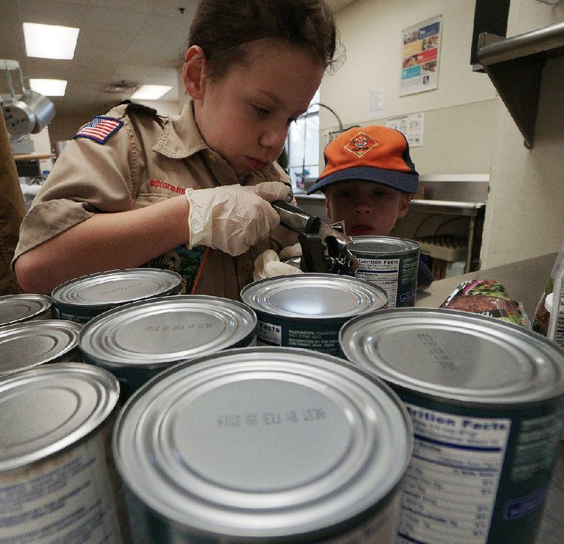 Luke Siria, 12, tries to open some canned goods and Michael Robbins, 7, looks on as they prepare lunch for people Saturday at the Our House shelter in Little Rock in honor of Patrick Wilson, a fellow Scout who died this fall.
