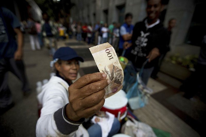 A street vendor inspects the authenticity of a 100-bolivar note as people stand in line outside a bank to deposit the notes Tuesday in Caracas, Venezuela.