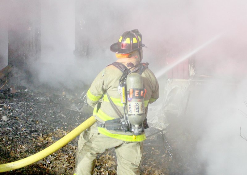 Keith Bryant/The Weekly Vista Bella Vista firefighter-paramedic William Coker sprays water on the burning house on Ciemny Lane Tuesday, Dec. 6.