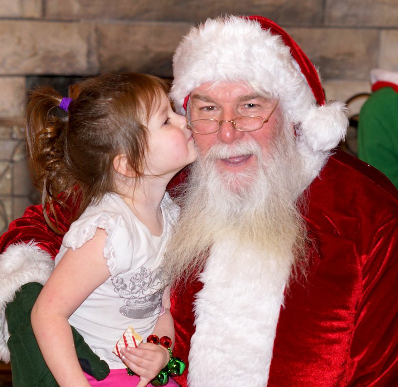 Photo by Randy Moll Skylar Binham, 3, gave Santa a kiss on the cheek when she visited with him at the Gentry Chamber of Commerce office on Saturday. Children visited with Santa for several hours on Saturday afternoon before the annual evening Christmas Parade on Gentry&#8217;s Main Street.