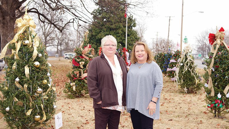 Sherry Fowler, vice president, special assets officer for Rivertown Bank, left, and Tanya Hendrix, executive director for the Dardanelle Area Chamber of Commerce, pose among the sponsored Christmas trees outside the Yell County Courthouse in Dardanelle.