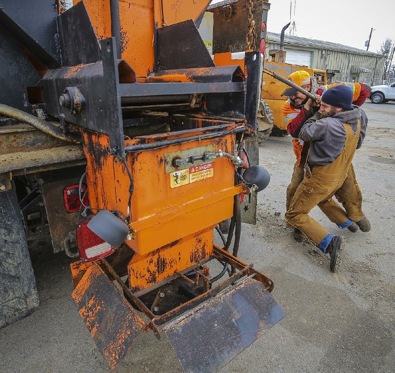 Highway Department workers Benjie McKenzie, (left) and Dustin McCool tighten chains securing a salt-spreading unit to a dump truck at a work yard Friday in North Little Rock as crews prepare for possible dicey weather during the weekend. 