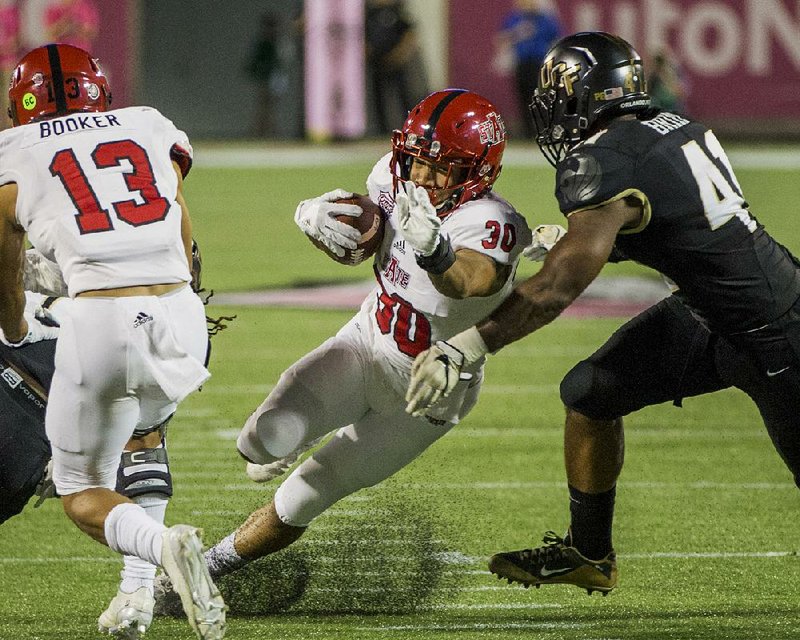 Arkansas State running back Johnston White (center) runs past Central Florida linebacker Demeitre Brim in Saturday night’s Cure Bowl in Orlando, Fla. The Red Wolves had just 29 yards rushing, but they had more than enough to beat the Knights 31-13.