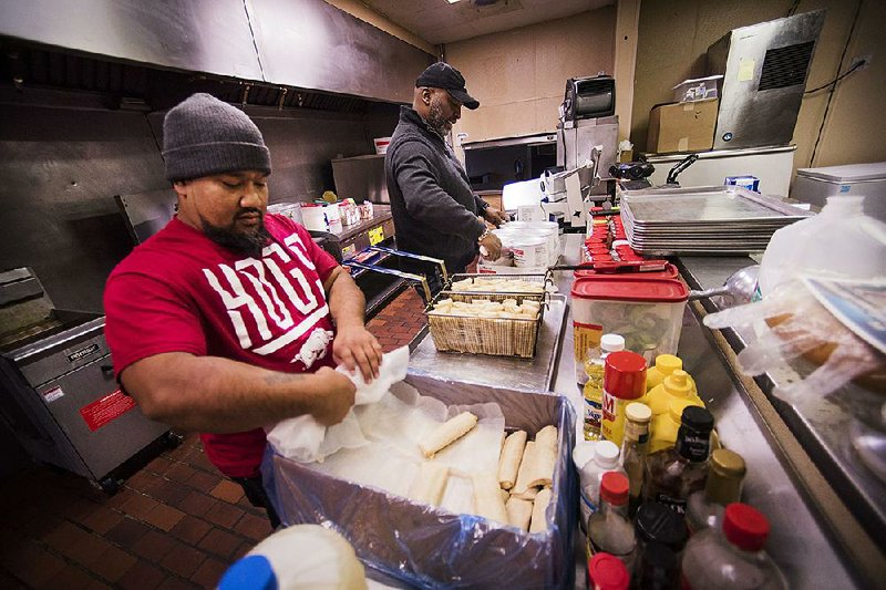 Moston Swington (left) cooks burritos as Edward Whitfield, director of the Promise Land Food Program, works Friday to cook vegetables in a kitchen they rent in Springdale.
