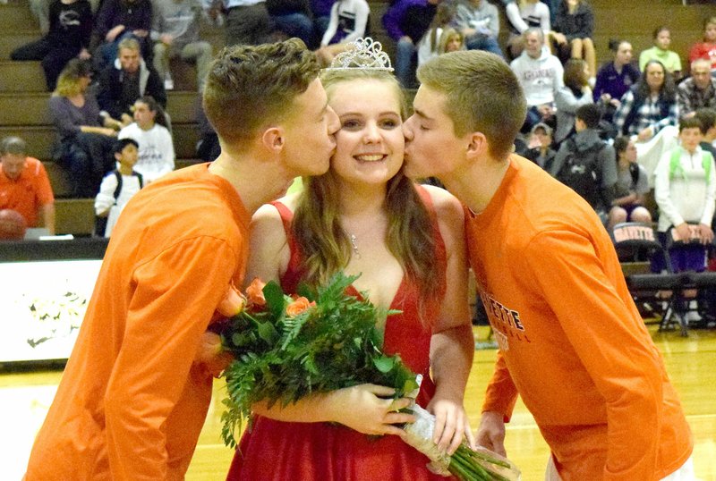 Photo by Mike Eckels Elizabeth McKenzie (center) receives kisses from her escorts, Kelton Trembley (left) and Seth Duke (right), after her coronation as the 2016 Basketball homecoming queen at Lion Field House in Gravette Dec. 16.