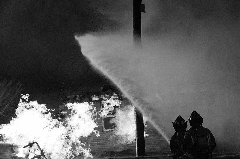 LYNN KUTTER ENTERPRISE-LEADER Firefighters from multiple fire departments kept a steady stream of water on the natural gas fire that ignited Friday afternoon when a car hit a gas main on U.S. 62 in Farmington.