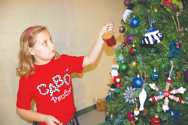 Cailynn Stone, 8, a third-grader at Central Elementary School in Cabot, places a drum ornament on one of the Christmas trees the school decorated and donated to a local family.