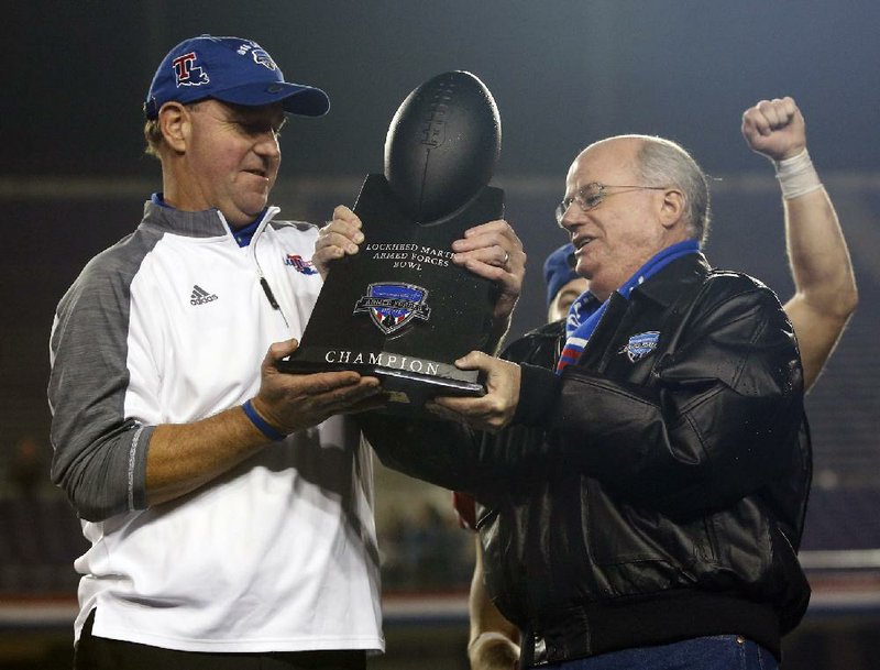 Louisiana Tech Coach Skip Holtz (left) accepts the Armed Forces Bowl championship trophy from Lockheed Martin vice president of aeronautics Orlando Carvalho on Friday after the Bulldogs defeated Navy 48-45 in Fort Worth.