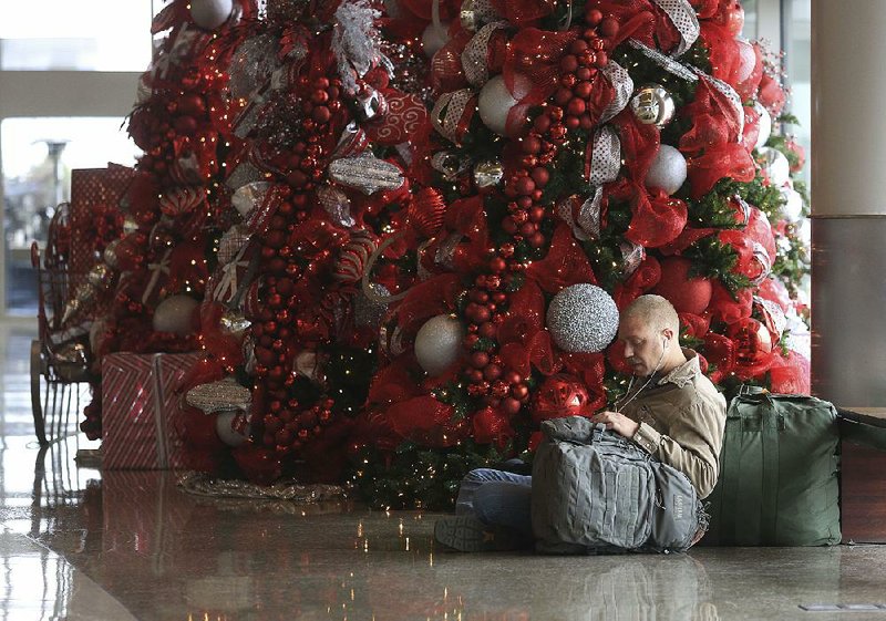 Lamont Wood waits next to a Christmas tree Friday afternoon for his flight to Kansas City, Mo., at Bill and Hillary Clinton National Airport/ Adams Field in Little Rock. Wood, who is training at Little Rock Air Force Base in Jacksonville, was traveling home for the holidays.