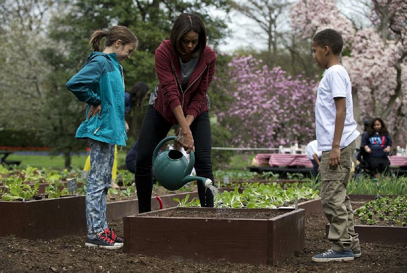 First lady Michelle Obama waters a bed of vegetable seeds with visiting students Nare Kande and Marley Santos on the South Lawn of the White House in this 2015 file photo.