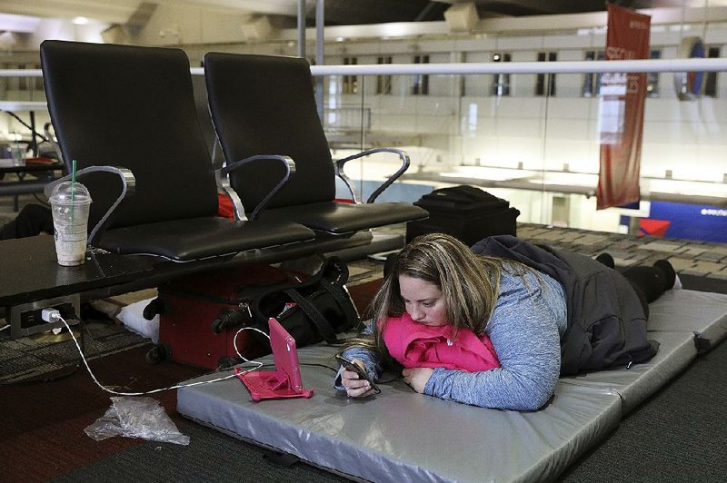 Chelsey Kalmback, 29, plays on her phone Monday at Minneapolis-St. Paul International Airport while waiting for a rescheduled flight to North Dakota after several flights were delayed or canceled mostly because of weather.

