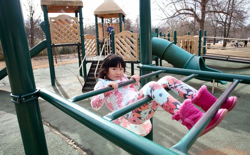 Jiana Hu, 6, hangs on one of the sets of playground equipment Wednesday at Wilson Park in Fayetteville. The city is investing $600,000 in improvements at the park that will include removing two playgrounds and replacing them with new equipment, adding a new musical playground and adding a new parking lot. The current playground equipment is about 20 years old. The work should be completed by the middle of 2017.