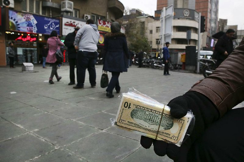 A money changer holds Iranian and U.S. banknotes Monday in downtown Tehran. The value of Iran’s currency has fallen 450 percent in the past 10 years.