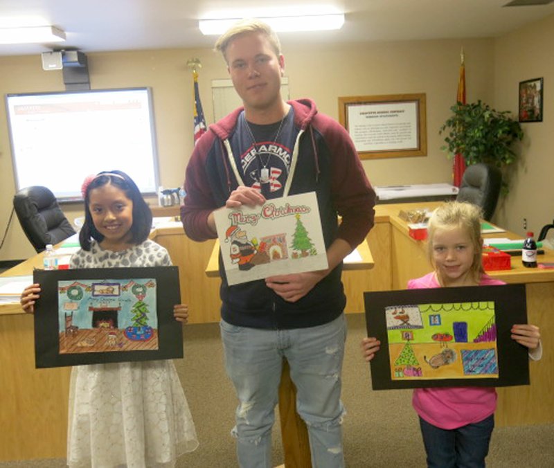 Photo by Susan Holland Young artists at Gravette schools were invited to submit artwork to be used as designs for the school district&#8217;s annual holiday greeting cards. Winners had their drawings printed on the cards and were honored at the December meeting of the Gravette school board. Each received a packet of cards to send to their friends and family. Pictured here with their original drawings are Emily Lopez, 4th-grader, Gravette Upper Elementary; Jason Dubach, 11th-grader, Gravette High School, a foreign exchange student from Switzerland; and Kennedy Flynt, 2nd-grader, Glenn Duffy Elementary School. Jaelen Wangaard, 7th-grader, Gravette Middle School, was not present.