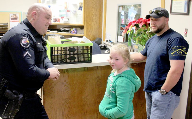 Keith Bryant/The Weekly Vista Bella Vista police officer Justin Green, left, thanks Apple Glen fourth-grader Abby Ward and her father Jared Gully, who brought a basket of snack bags from her class for Bella Vista officers.