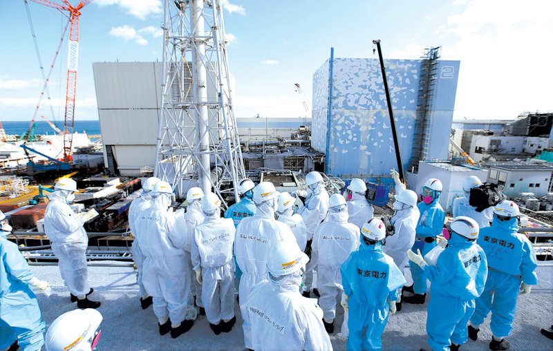 Reporters and photographers are briefed by Tokyo Electric Power Co. employees near the No. 1 and No. 2 reactor buildings at the utility’s Fukushima nuclear power plant during a tour in February. Dismantling the nuclear reactors, wrecked by the 2011 earthquake and tsunami, will cost about $68 billion. 