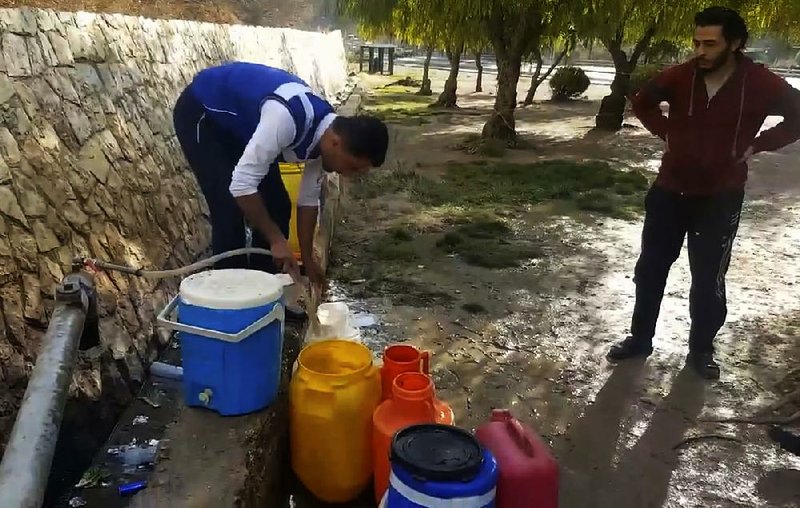 A Syrian resident fills up buckets with spring water from a pipe on the side of the road in Damascus.