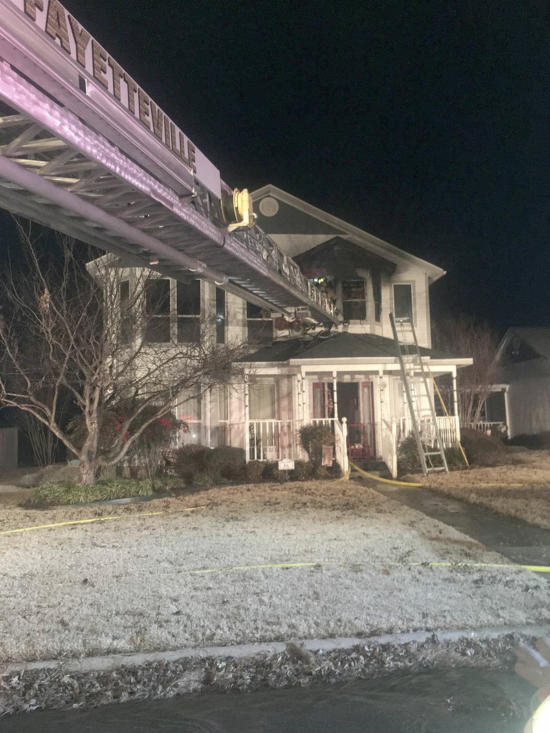 LYNN KUTTER ENTERPRISE-LEADER Firefighters use the ladder truck from Fayetteville Fire Department to access the second floor of this home in Farmington. Officials believe the fire started in the bathroom of the master bedroom.