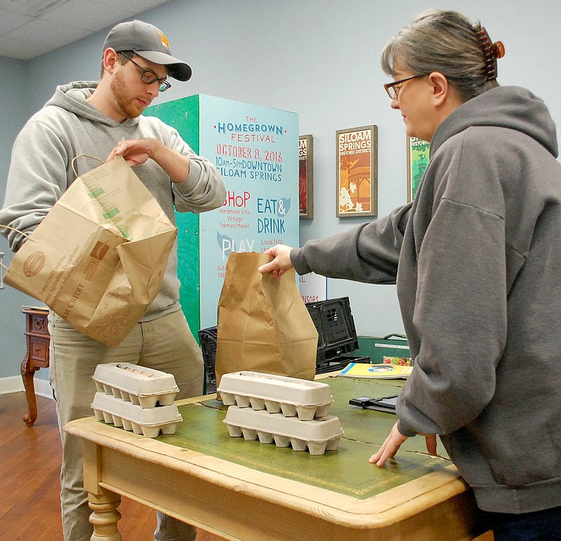 Janelle Jessen/Herald-Leader Farmers Market manager Stacey Hester, right, handed Jason Kingsley his online Farmers Market order on Saturday morning. Customers can order online Sunday through Thursday and pick up their items at the Main Street Siloam Springs office on Saturday morning.