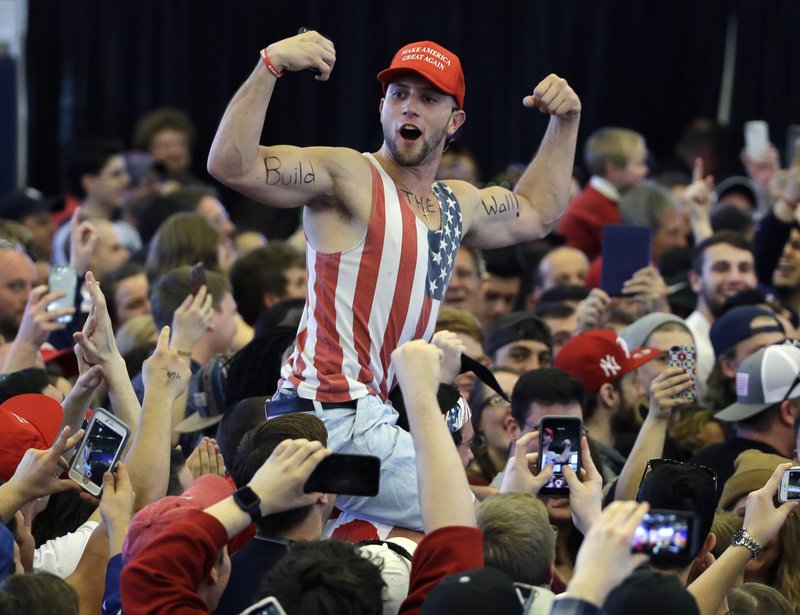 In this April 15, 2016, file photo, a Donald Trump supporter flexes his muscles with the words "Build The Wall" written on them as Trump speaks at a campaign rally in Plattsburgh, N.Y. 